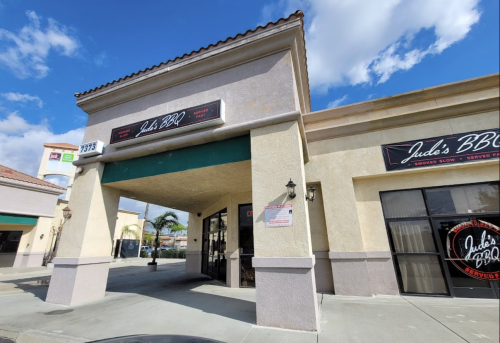 Exterior view of Jude's BBQ restaurant, featuring a sign and entrance, with a clear blue sky in the background.