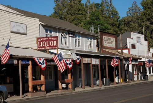 Historic buildings line a street, adorned with American flags, in a quaint mountain town.