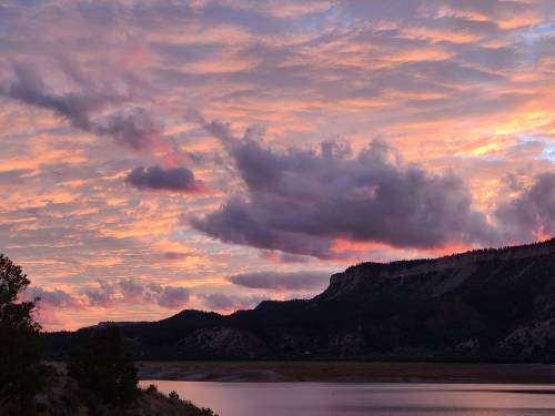 A vibrant sunset over a lake, with colorful clouds and mountains in the background.