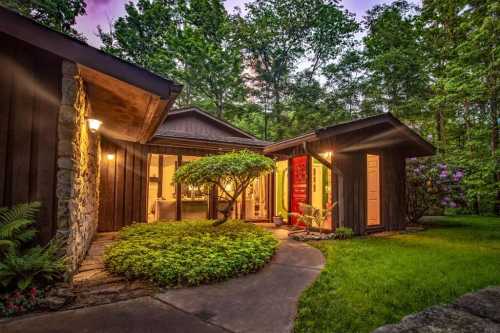 A cozy, modern home surrounded by lush greenery, with warm lights glowing from the windows at dusk.