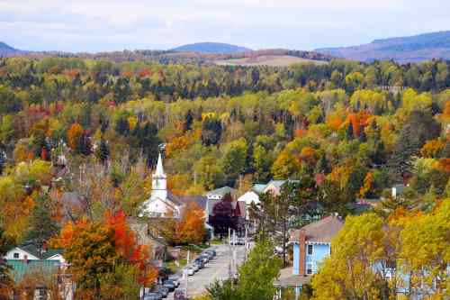 A scenic view of a small town surrounded by vibrant autumn foliage and rolling hills, featuring a church steeple.