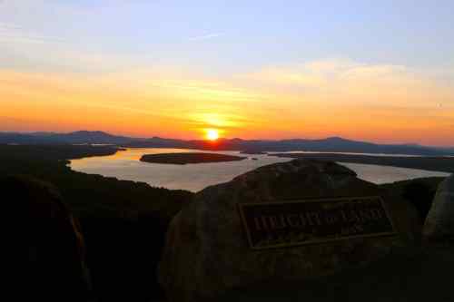 Sunset over a river and mountains, with a sign reading "Height of Land" in the foreground.