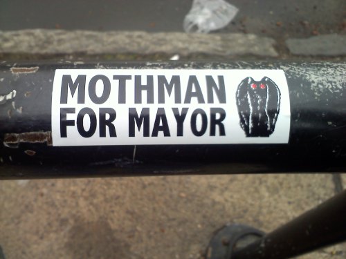 Sticker on a pole reads "Mothman for Mayor" with an illustration of Mothman.