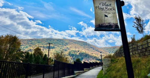A scenic pathway leads to mountains under a blue sky, with a sign for "Visit Flag Rock" visible.