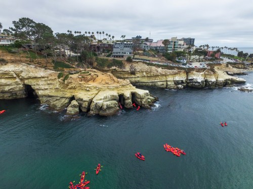 Aerial view of La Jolla coastline with cliffs, homes, and kayakers in the water on a cloudy day.