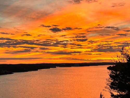 A vibrant sunset over a calm lake, with orange and pink hues reflecting on the water and clouds scattered in the sky.