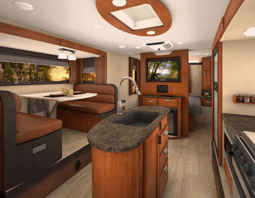 Interior of a modern RV featuring a kitchen, dining area, and living space with warm wood tones and natural light.