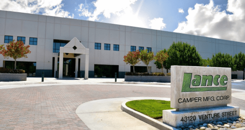 Exterior view of Lance Camper Manufacturing Corp building with a sign and landscaped entrance on Venture Street.