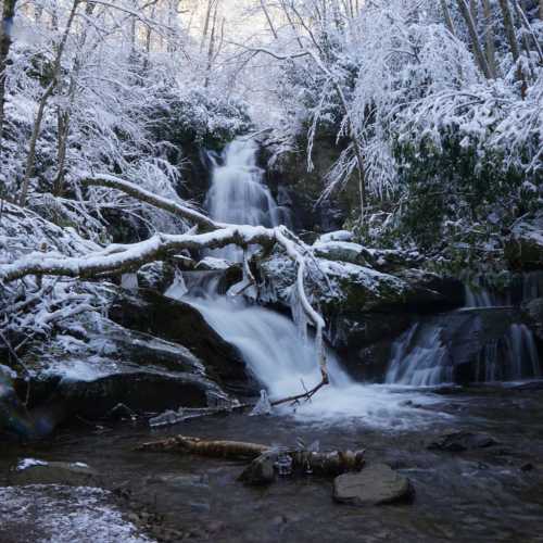 A serene winter scene featuring a snowy waterfall surrounded by trees and a rocky landscape.