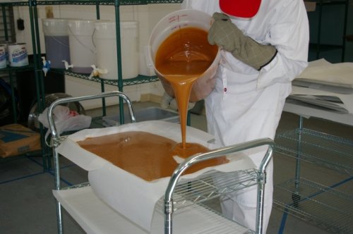 A person in protective gear pours a thick, brown liquid into a tray in a workshop setting.
