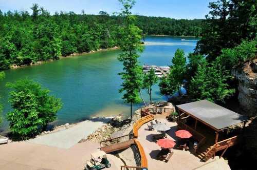 Scenic view of a lake surrounded by greenery, featuring a wooden deck with umbrellas and boats docked nearby.