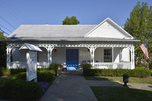 A charming white house with a blue door, decorative porch, and American flag, surrounded by greenery and flowers.