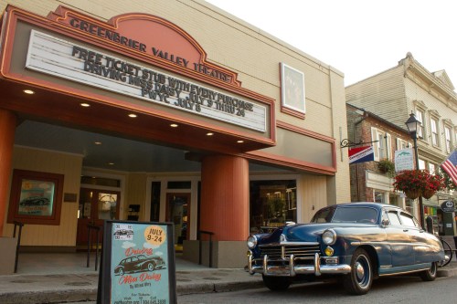 A vintage blue car parked in front of the Greenbrier Valley Theatre, featuring a marquee with upcoming events.