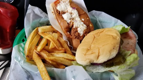 A basket with a hot dog topped with sauce, a hamburger with lettuce and pickles, and a side of French fries.