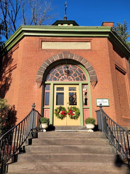 A brick building with a decorative entrance, featuring a green roof and holiday wreaths on the door.