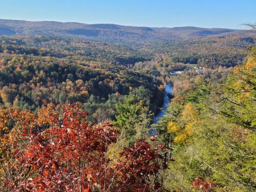 A scenic view of a river winding through colorful autumn foliage and rolling hills under a clear blue sky.
