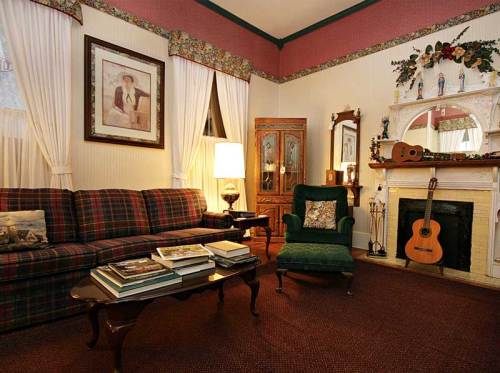 Cozy living room with a plaid sofa, green armchair, guitar, and decorative fireplace. Warm, inviting atmosphere.