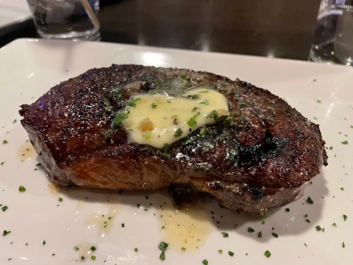 A perfectly cooked steak topped with a pat of butter and garnished with chopped herbs, served on a white plate.