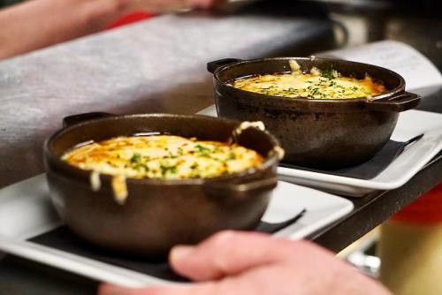 Two small, black ceramic bowls of baked cheese dish, garnished with herbs, on white plates.