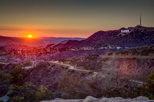 Sunset over hills with the Hollywood sign in the distance, casting a warm glow on the landscape.