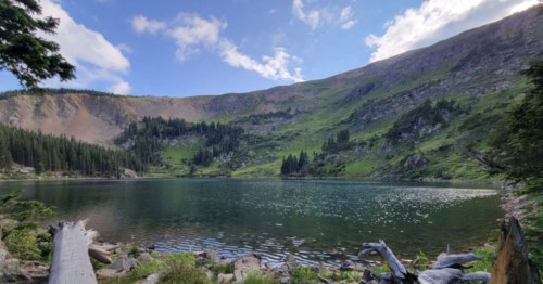A serene lake surrounded by lush green hills and trees under a partly cloudy sky.