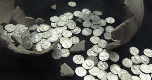 A broken pot spills ancient silver coins and fragments onto a dark surface.