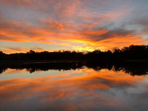 A serene sunset over a calm lake, with vibrant orange and pink hues reflecting on the water's surface.
