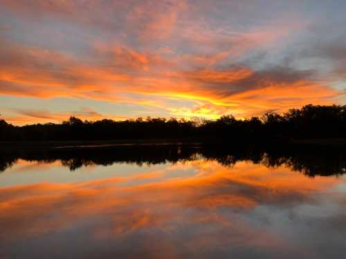 A serene sunset over a calm lake, with vibrant orange and pink hues reflecting on the water's surface.