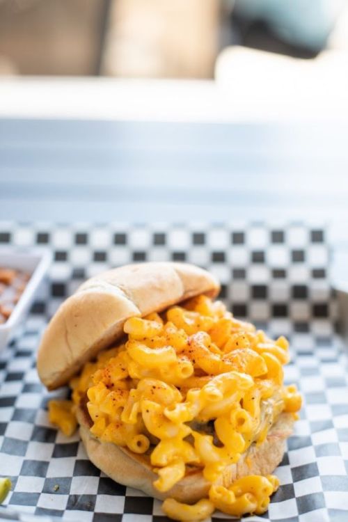 A sandwich overflowing with macaroni and cheese, served on a checkered paper.