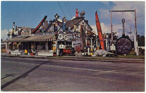 A quirky souvenir shop with colorful decorations, large signs, and a giant frying pan outside, set along a road.