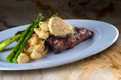 A plated meal featuring grilled steak, asparagus, and creamy potato salad with a dollop of herb butter on top.