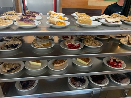 A display of various desserts on plates, including pies and cakes, arranged on metal shelves.