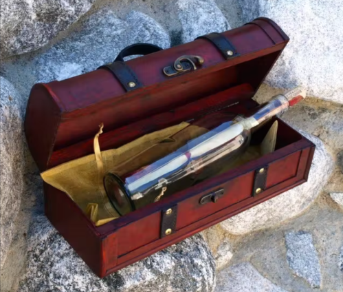 A red wooden box with a bottle inside, resting on a stone surface. The bottle is sealed and partially visible.