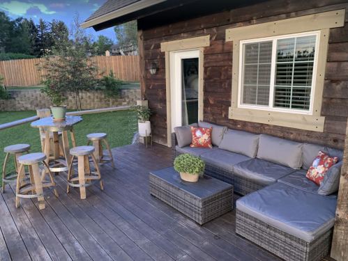 Cozy outdoor patio with a sectional sofa, coffee table, and bar-height table with stools, surrounded by greenery.