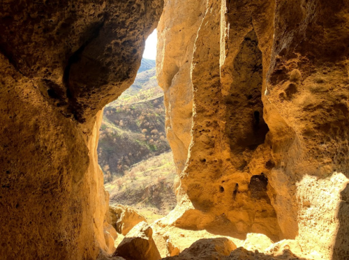 A view from inside a cave, showcasing rugged rock formations and a glimpse of the landscape outside.