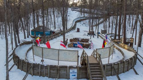A snowy landscape featuring a winding toboggan run surrounded by trees and flags from various countries.