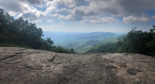 A panoramic view of rolling green mountains under a cloudy sky, seen from a rocky overlook.