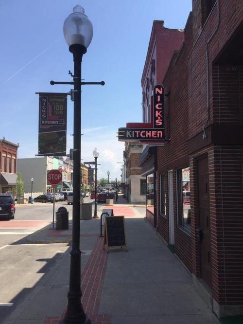 A street view featuring Nick's Kitchen sign, a lamp post, and a stop sign, with buildings lining the road.