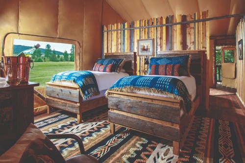 Cozy bedroom with two beds, rustic decor, colorful blankets, and a scenic view through a large window.