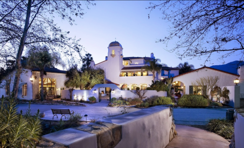 A beautiful Spanish-style building at dusk, surrounded by lush greenery and soft lighting.