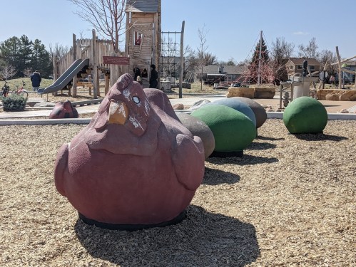 Colorful, oversized rock sculptures resembling animals in a playground with slides and trees in the background.
