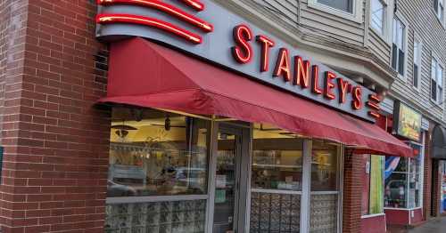 Exterior of Stanley's restaurant with a red awning and neon signage, featuring brick walls and large windows.