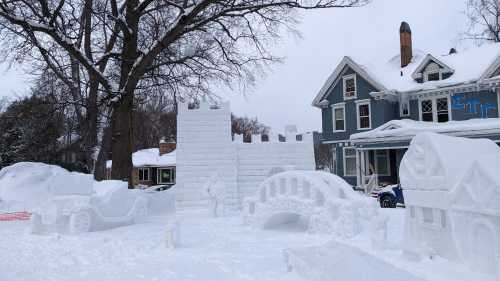 A snowy scene featuring a large snow castle, bridge, and various snow sculptures in a residential area.