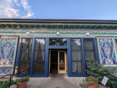 A colorful building facade with intricate tile work, featuring large windows and a welcoming entrance.