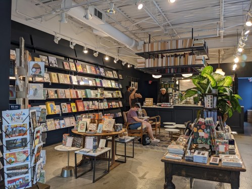 A cozy bookstore with shelves of books, a seating area, and customers browsing in a well-lit space.
