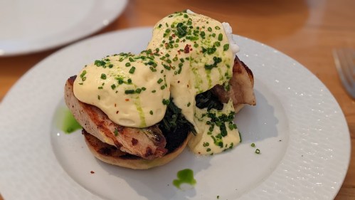 A plate of eggs Benedict featuring poached eggs, hollandaise sauce, and chives on toasted English muffins.