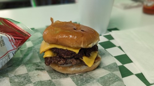 A cheeseburger with two layers of melted cheese on a toasted bun, served on a green and white checkered paper.