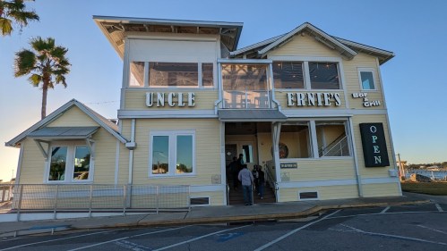 Exterior of Uncle Ernie's Bar & Grill, a yellow building with palm trees, featuring an "OPEN" sign and waterfront view.