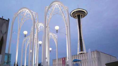 The Space Needle stands tall beside illuminated arches and lamps against a twilight sky.