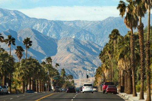 A scenic road lined with palm trees, leading towards mountains under a clear blue sky.